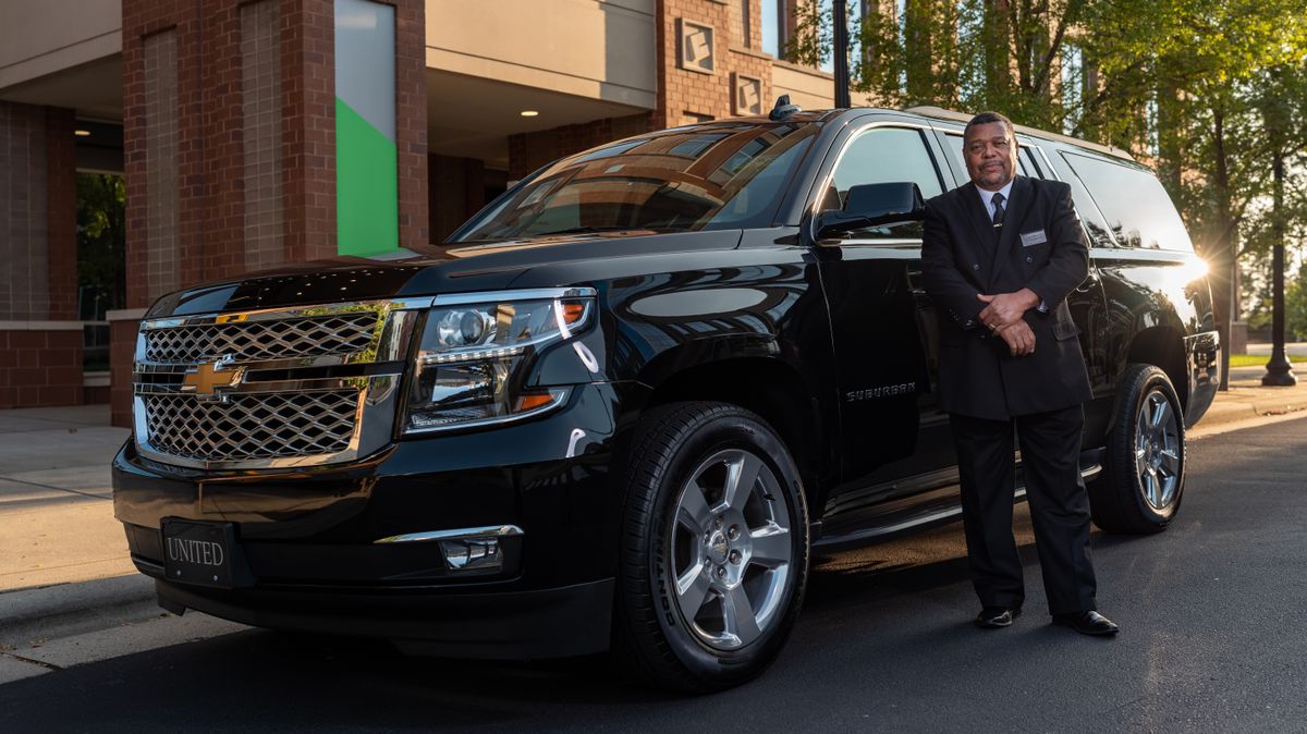Uniformed chauffeur standing beside a corporate vehicle