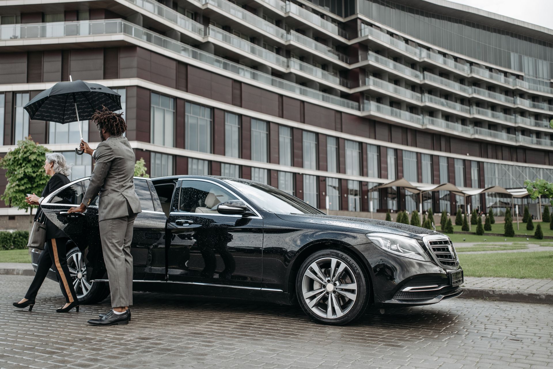Chauffeur holding an umbrella as an executive steps out of a black luxury sedan